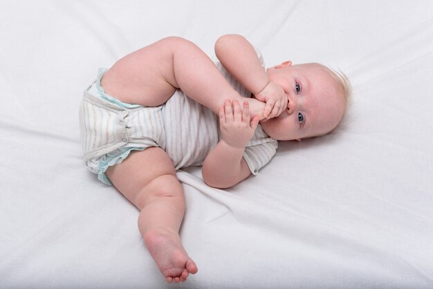 Petit bébé grignote son pied sur un lit blanc. Joli bébé de 3 mois. Gymnastique pour le nouveau-né.