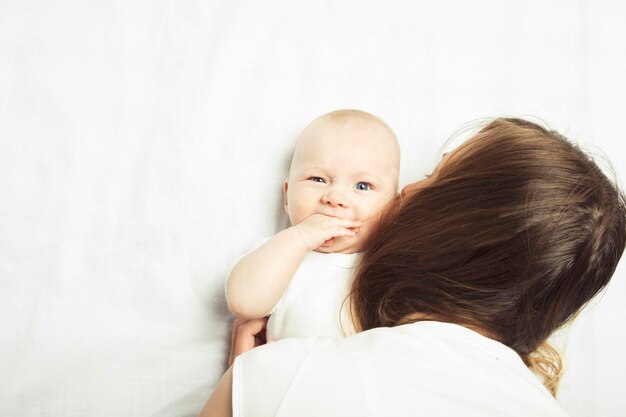 Petit bébé avec maman sur un lit avec un drap blanc. Mise à plat, vue de dessus.