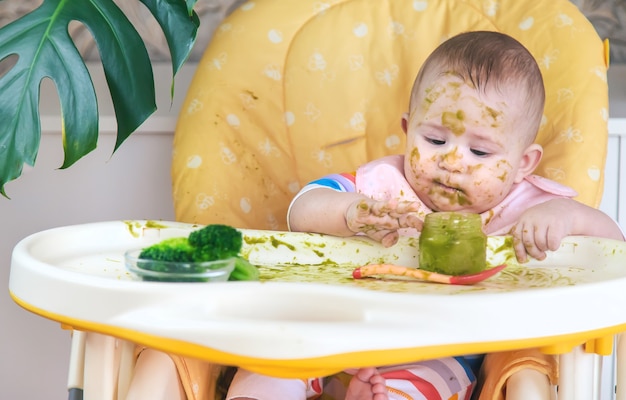 Le petit bébé mange lui-même de la purée de brocoli. Mise au point sélective. Gens.