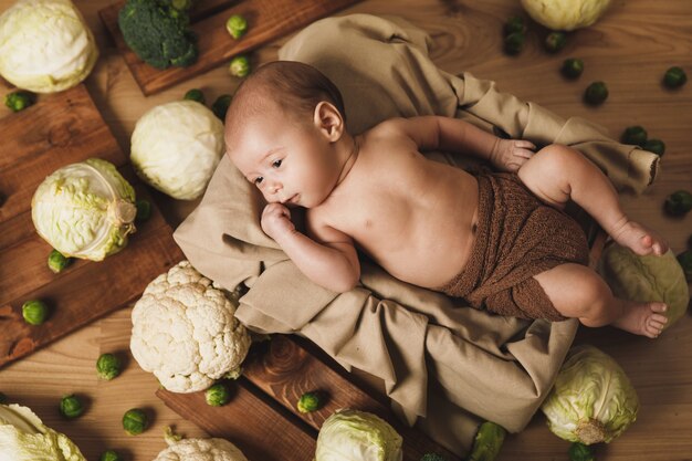 Un petit bébé mignon est couché dans la boîte avec beaucoup de choux différents autour