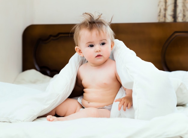 Un petit bébé mignon et mignon sourit sous une couverture blanche. portrait de bébé de 11 mois