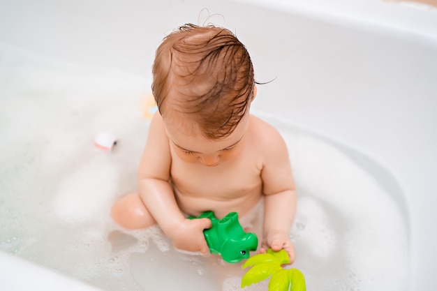 Petit bébé mignon prend un bain et joue avec des bulles de mousse et un jouet