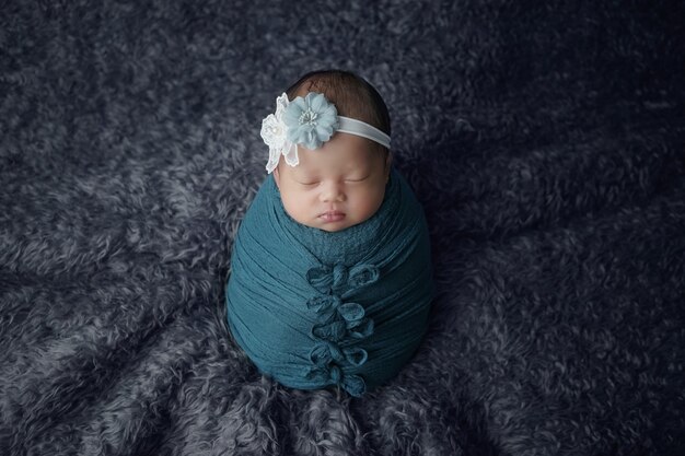 Le petit bébé nouveau-né enveloppé dans une écharpe bleue avec un bandage sur la tête se trouve sur une couverture douce