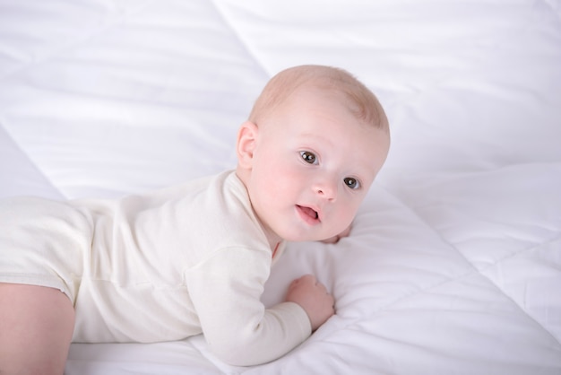 Petit bébé rampe sur le lit blanc.