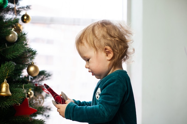 Petit bébé tenant un jouet de Noël avec un arbre de Noël dans ses mains. Nouvel an et Noël à la maison. Vacances d'hiver décorer l'arbre de Noël.