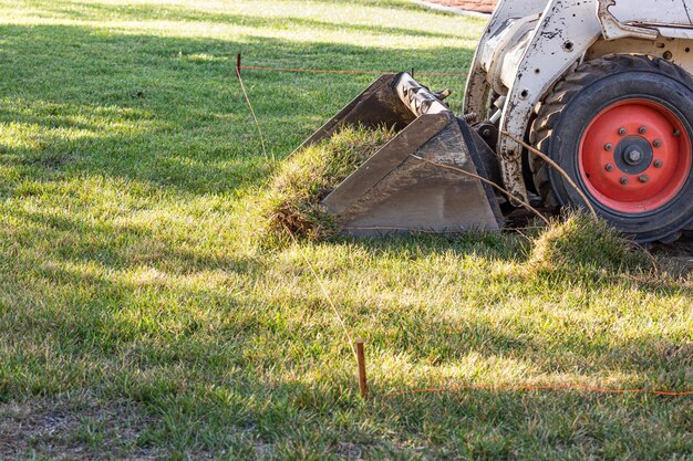 Un petit bulldozer enlève l'herbe de la cour pour préparer l'installation de la piscine