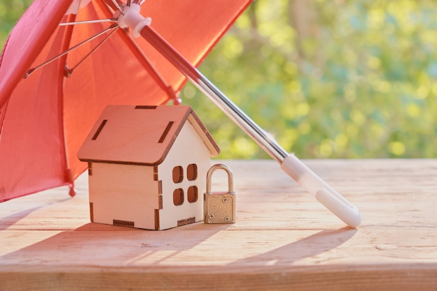 Petit cadenas, parapluie dôme rouge et modèle de maison en bois sur une surface de planche de bois, fond naturel vert, concept de protection immobilière, assurance