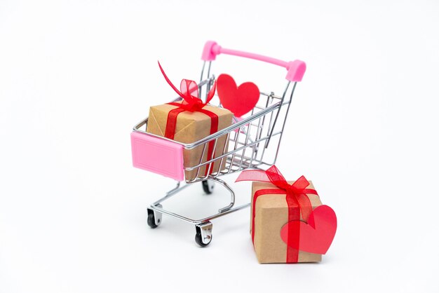Petit chariot d'épicerie avec des coffrets cadeaux sur une surface blanche. Offrez des cadeaux avec amour le jour de la Saint-Valentin
