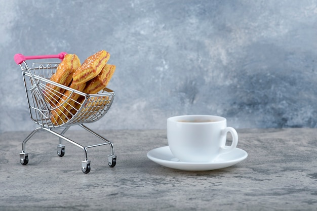 Un petit chariot rose de délicieux biscuits avec une tasse de thé chaud posé sur un motif en marbre.