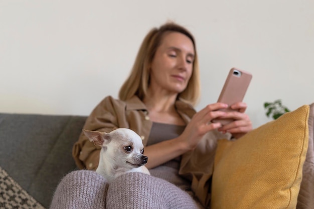 Petit chien assis sur les genoux d'une femme utilisant une application vétérinaire sur son téléphone