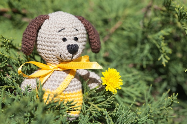 Un petit chien marron tricoté avec un ruban jaune dans le jardin d&#39;été. Jouet tricoté à la main, amigurumi