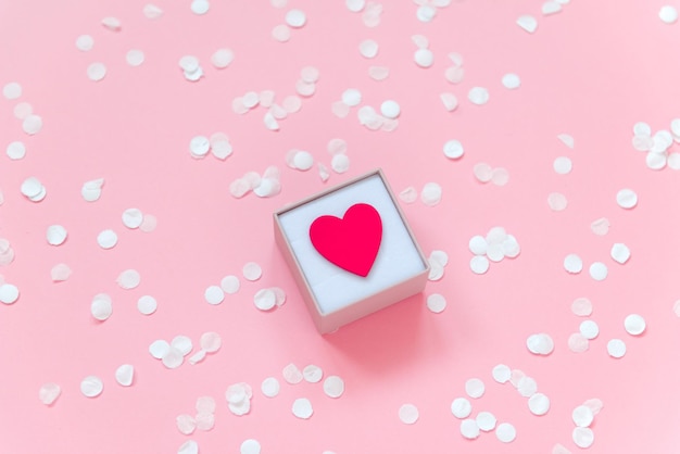 petit coeur rouge dans une boîte sur fond rose avec des confettis saint valentin concept mise à plat