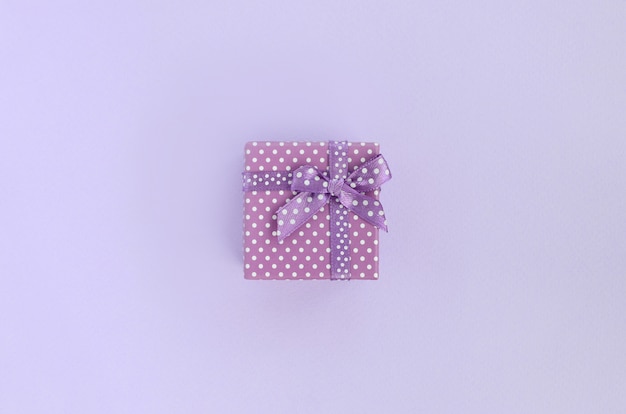 Un petit coffret violet avec ruban se trouve sur un fond violet.