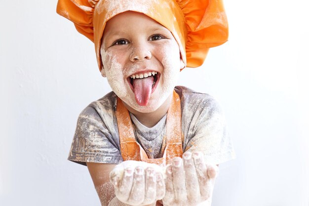 Photo un petit cuisinier joyeux avec de la farine dans les mains montre sa langue en gros plan