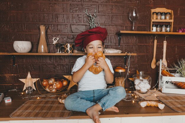 Petit cuisinier. Petit enfant portant une toque avec des pâtisseries, des petits pains, du pain et des bagels. Garçon mangeant un bagel.