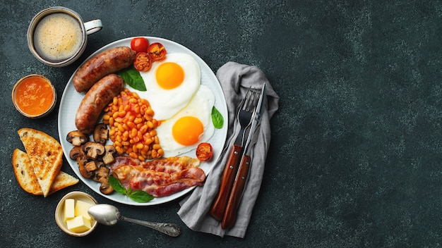 Petit-déjeuner anglais complet sur une assiette avec des œufs au plat, des saucisses, du bacon, des haricots, des toasts et du café. Vue de dessus.