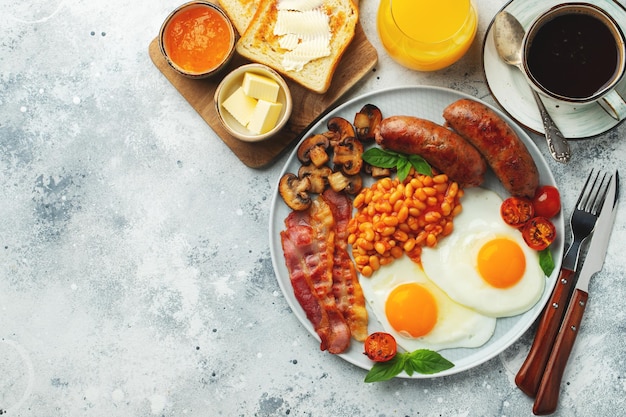 Petit déjeuner anglais complet sur une assiette avec des œufs frits, des saucisses, du bacon, des haricots grillés et du café sur un fond de pierre claire avec un espace de copie.