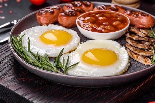 Petit-déjeuner anglais complet haricots œufs frits saucisses rôties tomates champignons sur une table en béton foncé avec du pain grillé