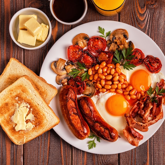 Petit-déjeuner anglais complet traditionnel avec des œufs au plat, des saucisses, des haricots, des champignons, des tomates grillées et du bacon sur fond de bois