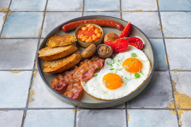 Petit-déjeuner anglais avec des œufs au plat saucisses bacon haricots toasts tomates et champignons fond de tuile...