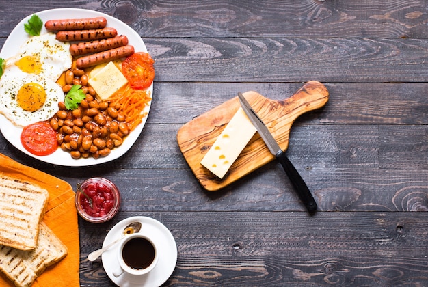 Petit déjeuner anglais. Oeufs sur plat saucisses haricots pain toasts tomates fromage sur un fond en bois