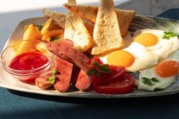 Petit-déjeuner anglais avec des œufs saucisses toasts français et quartiers de pommes de terre sur table grise