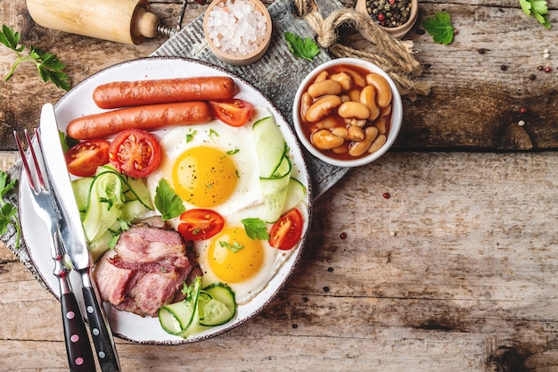 Petit-déjeuner anglais traditionnel avec des œufs au plat, du bacon, des haricots, du café et des saucisses sur une surface en bois, vue du dessus