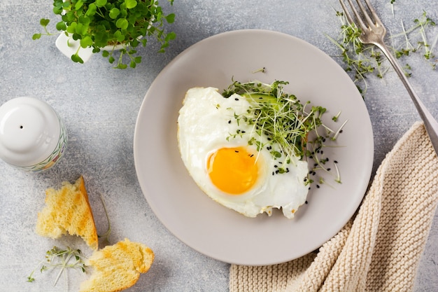 Petit-déjeuner anglais traditionnel avec des œufs au plat avec de la roquette microgreen dans une plaque en céramique grise sur une vieille table en béton gris. Vue de dessus.