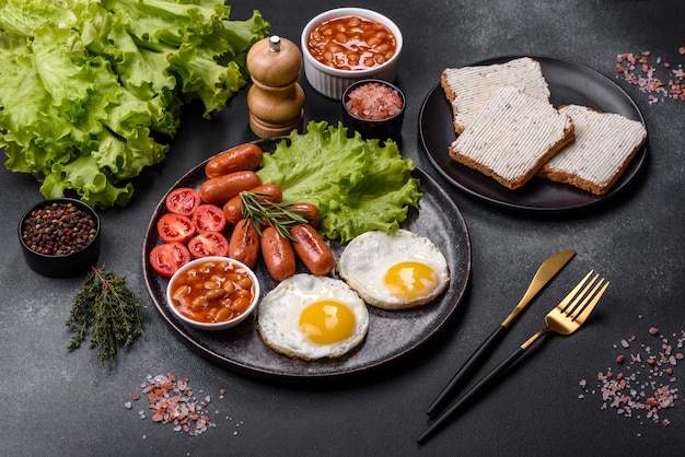 Petit-déjeuner anglais traditionnel avec des œufs, des saucisses grillées, des haricots, des épices et des herbes sur une plaque en céramique grise