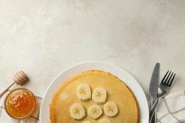 Petit-déjeuner avec assiette de fines crêpes à la banane et confiture sur une surface texturée blanche