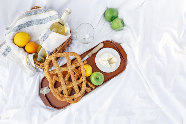 Petit déjeuner au lever du soleil, sur le drap blanc d'herbe avec un plateau avec fromage et vigne, pain sec, pomme, citron. humeur romantique, concept esthétique de style de vie lent, vue de dessus