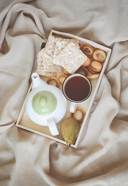 Petit-déjeuner au lit dans un plateau en bois avec des biscuits sucrés aux poires théière et tasse de thé