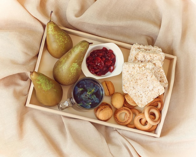 Petit-déjeuner au lit dans un plateau en bois avec poires confiture de poire bisquits biscuits sucrés théière et tasse de thé bleu biologique de thaïlande anchan clitoria pois papillon