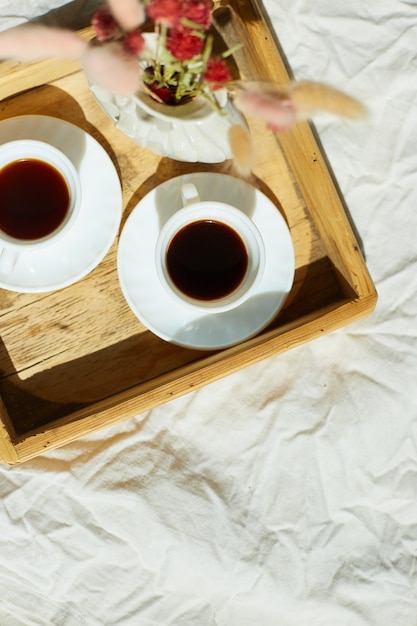 Petit-déjeuner au lit, essayez avec deux tasses de café et des fleurs au soleil à la maison, femme de chambre apportant un plateau avec petit-déjeuner dans la chambre d'hôtel, bon service