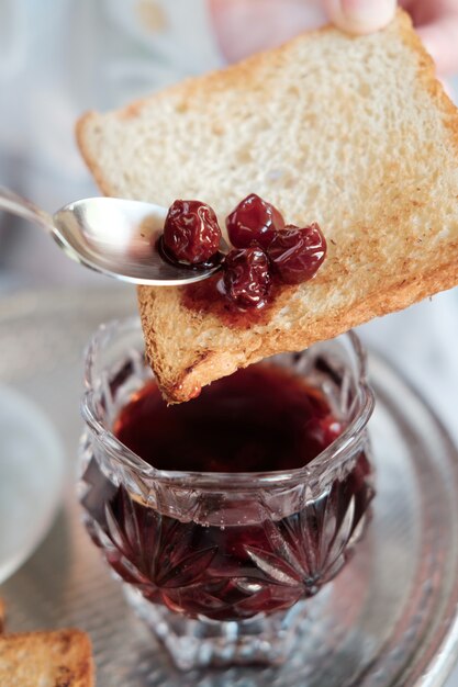 Petit déjeuner au lit à l'hôtel. Cuillère à soupe de confiture de cerises sur un toast.