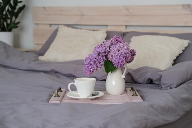 Petit-déjeuner au lit Plateau avec café et bouquet de lilas sur le lit dans la chambre