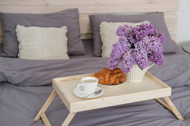 Petit-déjeuner au lit Plateau avec croissants au café et bouquet de lilas sur le lit dans la chambre