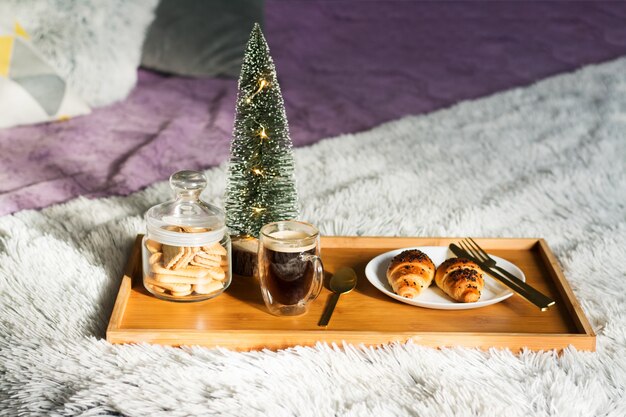 Petit déjeuner au lit avec tasse à café, croissants et biscuits sur plateau. Matin de noël