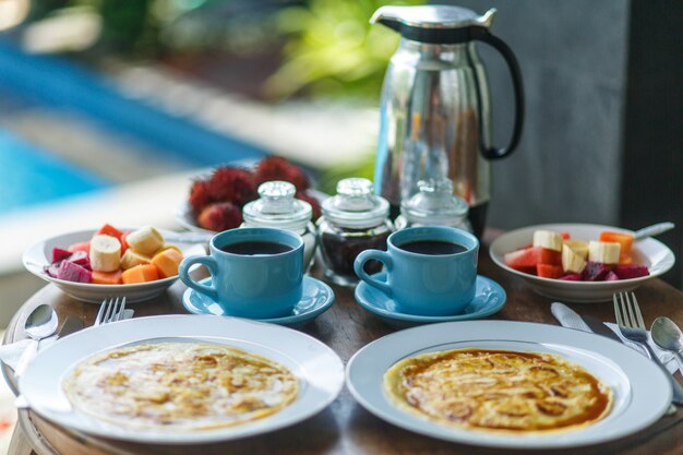 Petit déjeuner balinesse traditionnel avec deux tasses bleues de boisson chaude sur une table en bois.