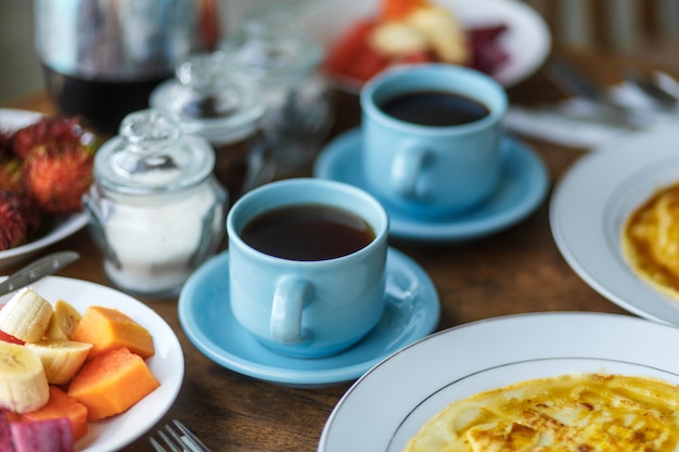 Petit-déjeuner balinesse traditionnel avec deux tasses bleues de boisson chaude sur table en bois.