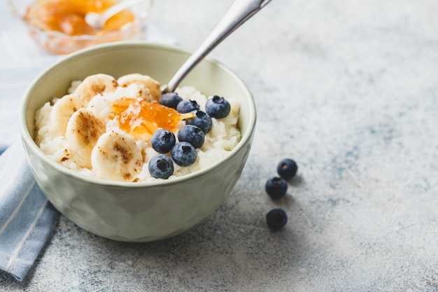 Petit-déjeuner avec bouillie de riz au lait avec bananes, confiture de myrtilles et d'orange, riz au lait crémeux ou riz au lait français dans un bol.