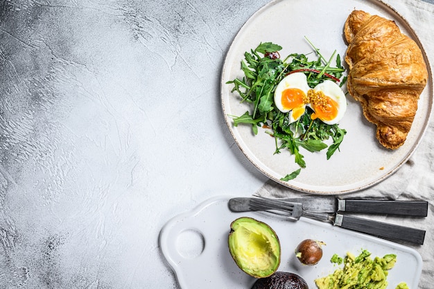 Petit déjeuner, brunch à l'avocat, roquette, croissant et œuf. Vue de dessus