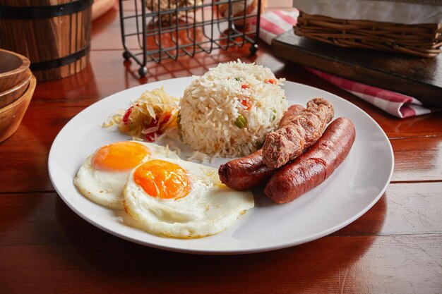 Petit-déjeuner brunch avec saucisses, riz frit et œufs servis dans un plat isolé sur fond bois vue latérale