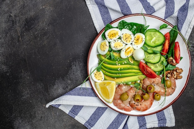 Petit-déjeuner cétogène Keto crevettes à faible teneur en glucides crevettes œufs de caille salade fraîche tomates concombres et avocat sur fond sombre régime céto vue de dessus