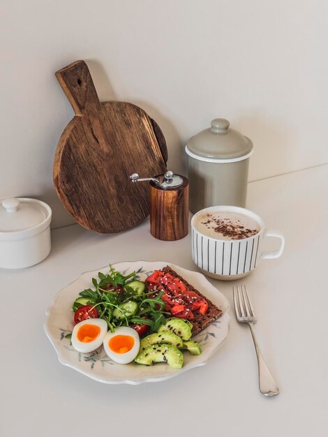 Un petit déjeuner chaleureux, un sandwich au saumon, une salade d'œufs bouillis et un cappuccino sur la table de la cuisine.