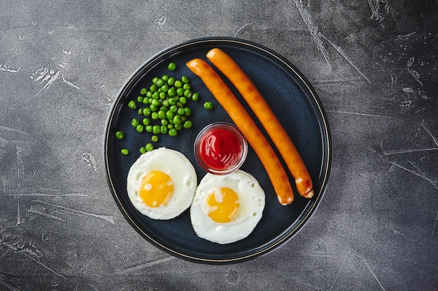 Petit-déjeuner classique composé de saucisses aux œufs frits et de pois verts sur un plat sur fond gris