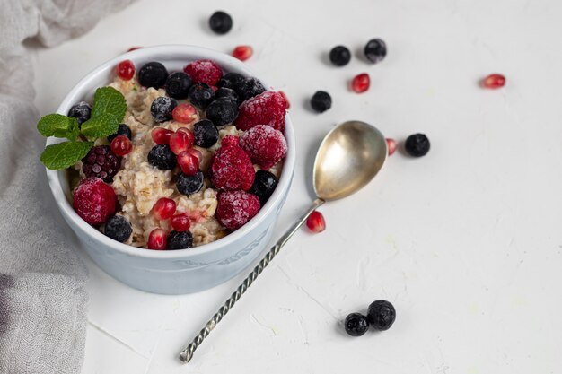 Petit déjeuner composé de flocons d'avoine, de noix et de fruits. Kiwi framboises mûres grenades amandes menthe décorer une assiette.