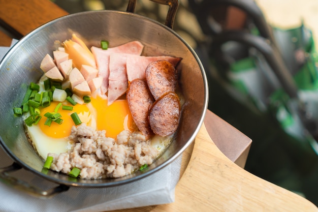 petit-déjeuner composé d'œufs au plat, de saucisses, de jambon et de porc haché dans une petite casserole