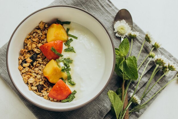 Photo le petit-déjeuner composé de yaourt muesli et de pêches se tient dans une assiette sur une serviette en lin