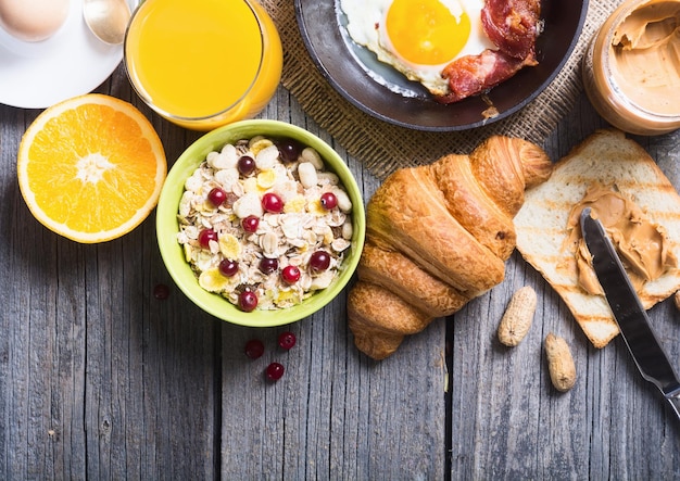 Photo petit-déjeuner comprenant du café, des œufs au plat, un croissant, du jus d'orange, du muesli et du pain